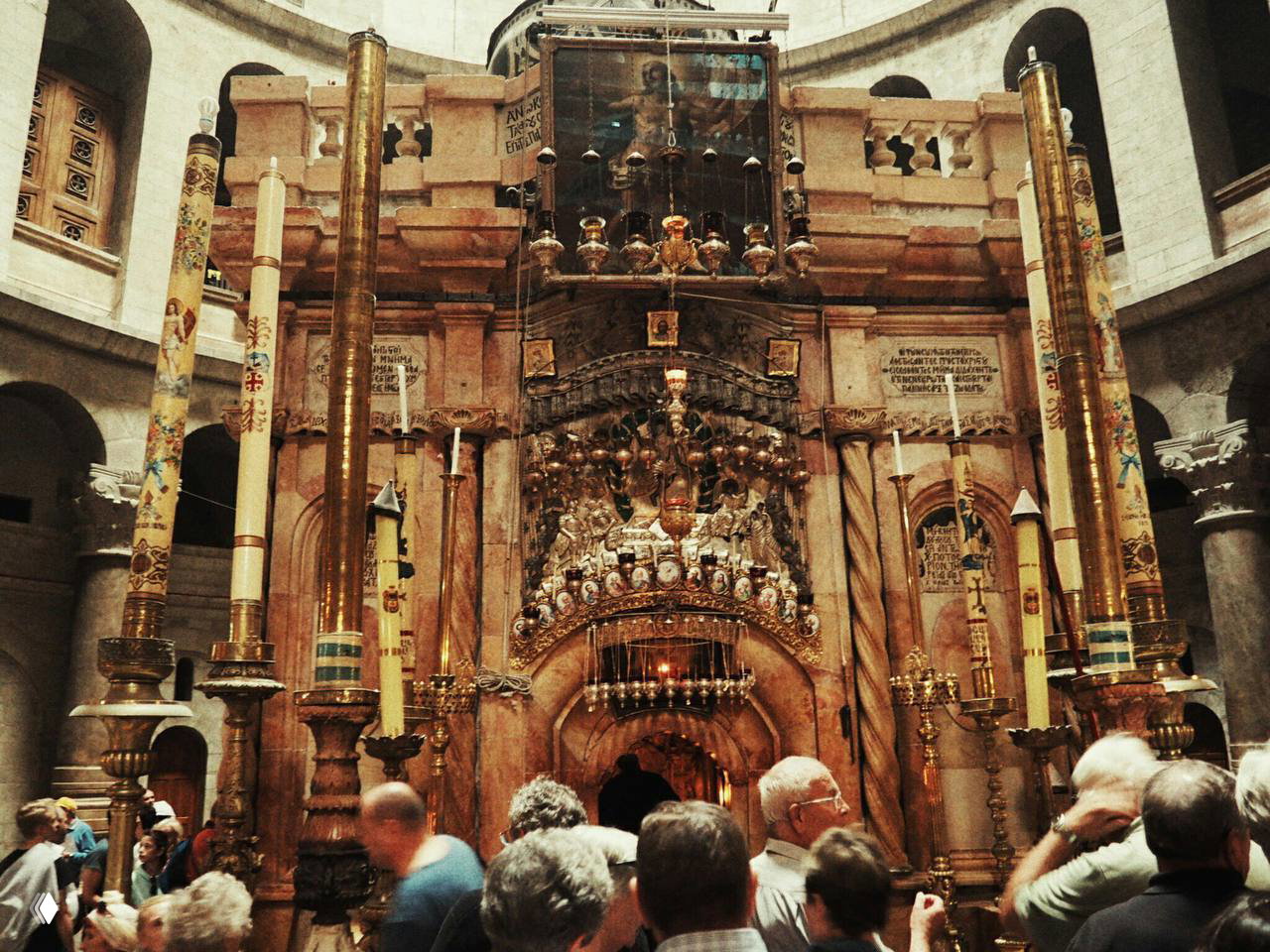 Интерьер Храма Гроба Господня: богато украшенная часть с подсвечниками и ритуальными элементами, паломники вокруг святыни.