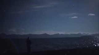 Ночное небо над Тибетом: силуэт человека у воды, звёзды и бледные световые пятна в небе — возможные атмосферные разряды.