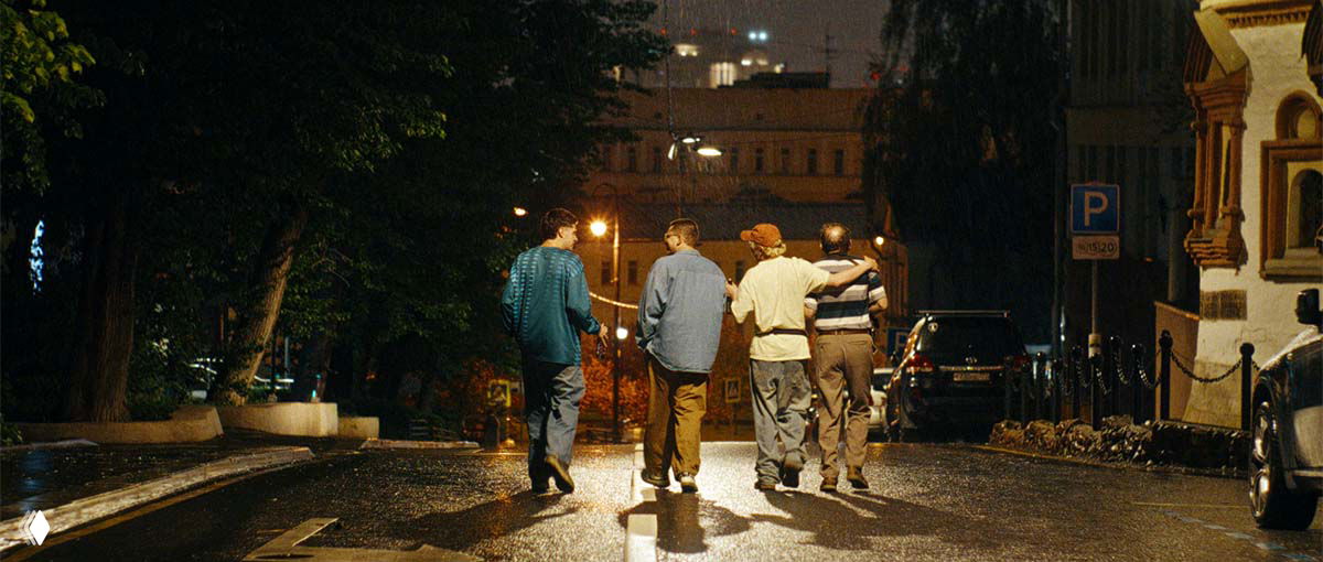 Ночной кадр фильма: четыре парня идут по мокрой улице спиной, атмосфера коммунального двора и дружеской компании.