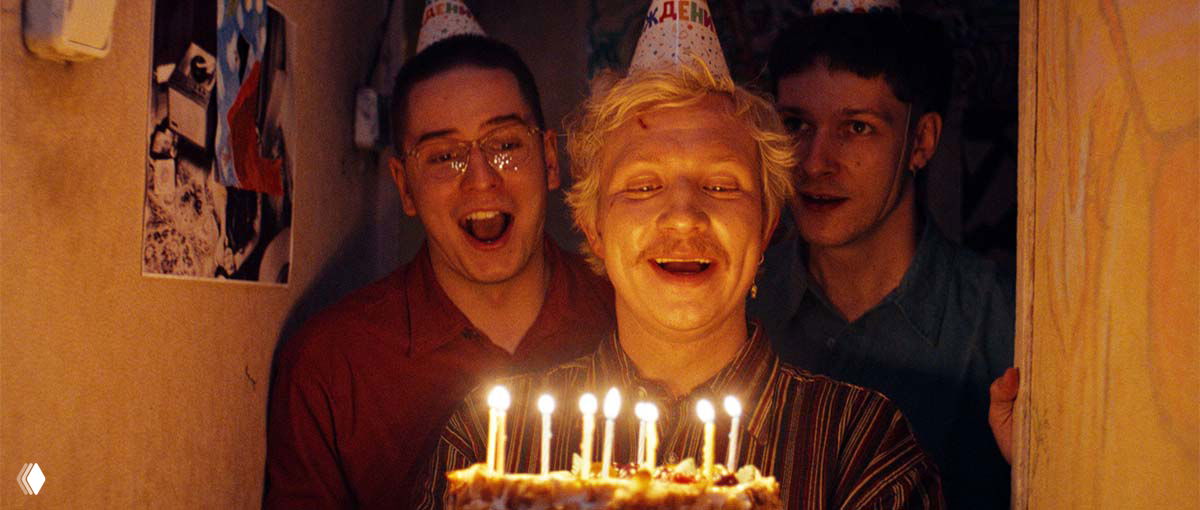 Тёплый кадр в коридоре коммуналки: трое героев поздравляют с тортом, свечи освещают их лица, ощущение искренней близости.