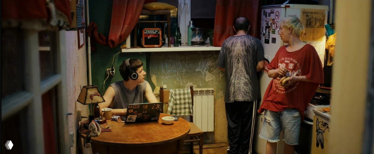 Интерьер коммунальной кухни: один за ноутбуком, другие готовят и общаются — визуализация бытовой, неотёсанной жизни героев.