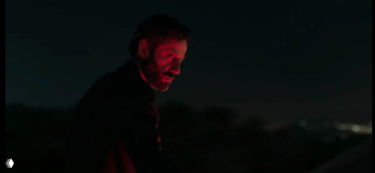 Крупный план мужчины в ночной сцене с драматическим красным освещением; напряжённый кадр подчёркивает внутреннюю борьбу героя.