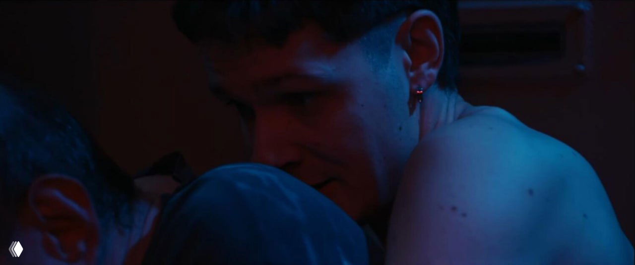 Крупный план молодого персонажа в полумраке: эмоциональная сцена близости и уязвимости между героями фильма.
