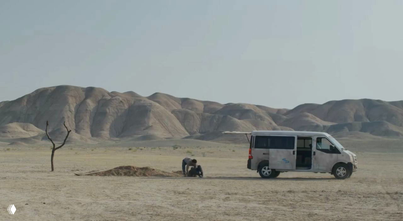 Широкий план пустыни с фургоном у одинокого дерева и людьми рядом, визуализация изоляции и пустоты в полотне фильма.