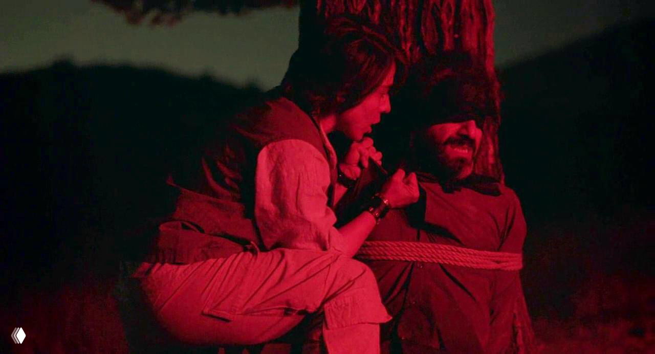 Ночная сцена в красных тонах: связанный мужчина и стоящий рядом персонаж создают ощущение угрозы и морального кризиса.