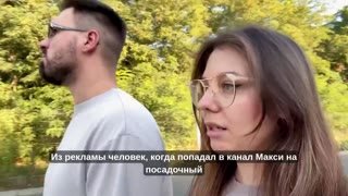 Кадр из видео: женщина в очках идёт рядом с мужчиной на фоне зелёных деревьев; на изображении видны субтитры о приходе человека из рекламы в канал Макси, разговорная сцена прогулки.