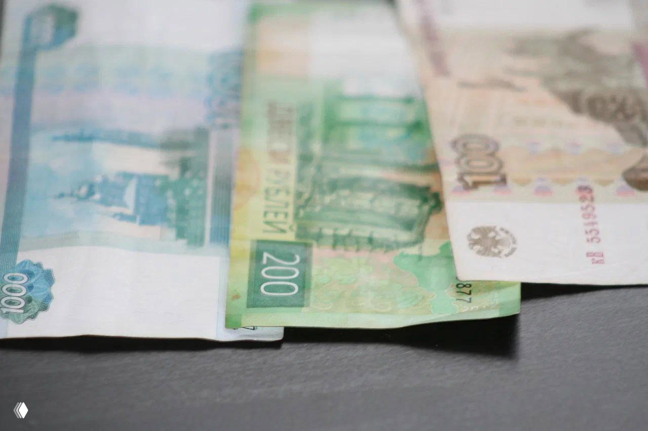 Разложенные на столе российские банкноты (тысяча, двести, сто рублей) как иллюстрация темы проблемной ипотеки и финансовых выплат.