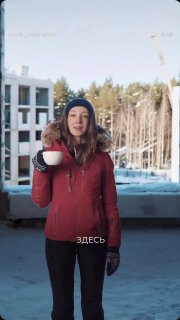 Девушка в зимней одежде с чашкой на фоне строящегося комплекса и леса — сцена оформления видеоконтента для демонстрации местоположения объекта.
