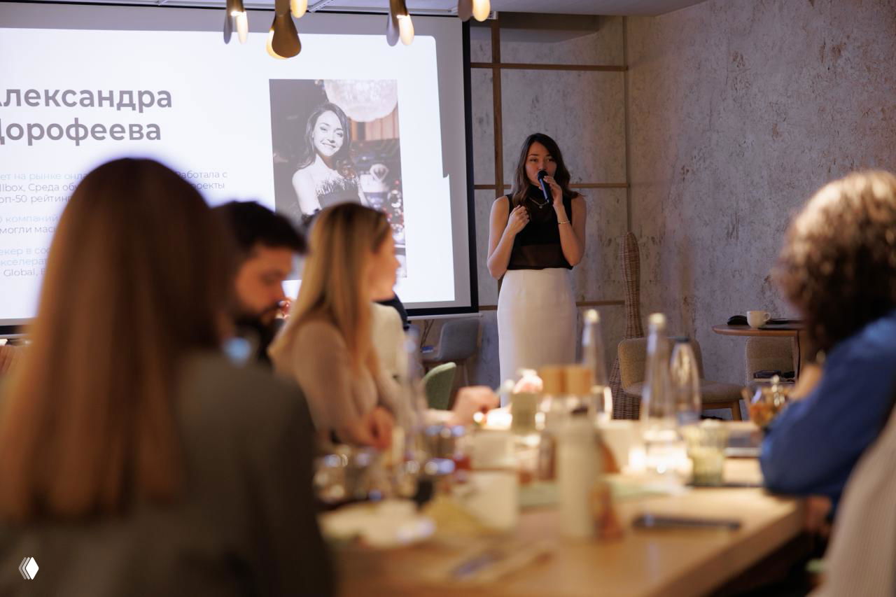 Спикер стоит у экрана, аудитория за столами обсуждает идеи; на заднем плане виден общий интерьер уютного гастрономического пространства в Москве.