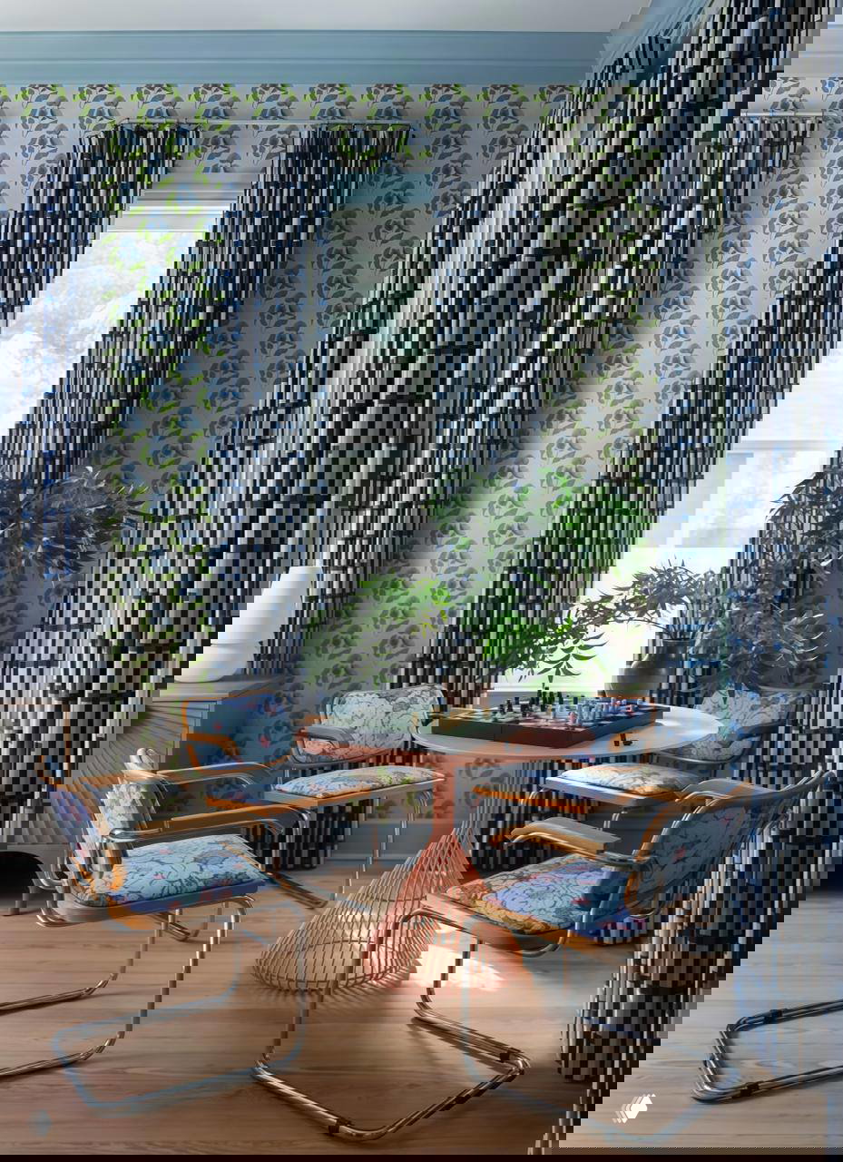 Интерьер с яркими шторами и обоями в цветочный рисунок, круглый стол с шахматами и четыре кресла — сочетание викторианского духа и современного прочтения.