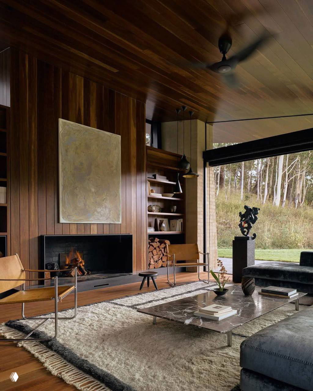 Интерьер гостиной с деревянной облицовкой стен и потолка, камином и крупными окнами, создающий тёплую и законченно художественную атмосферу.