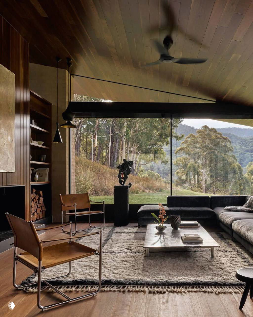 Просторная зона с панорамным окном, низким диваном и предметами дизайна на фоне открывающегося лесного вида — интерьер как самостоятельный художественный объект.