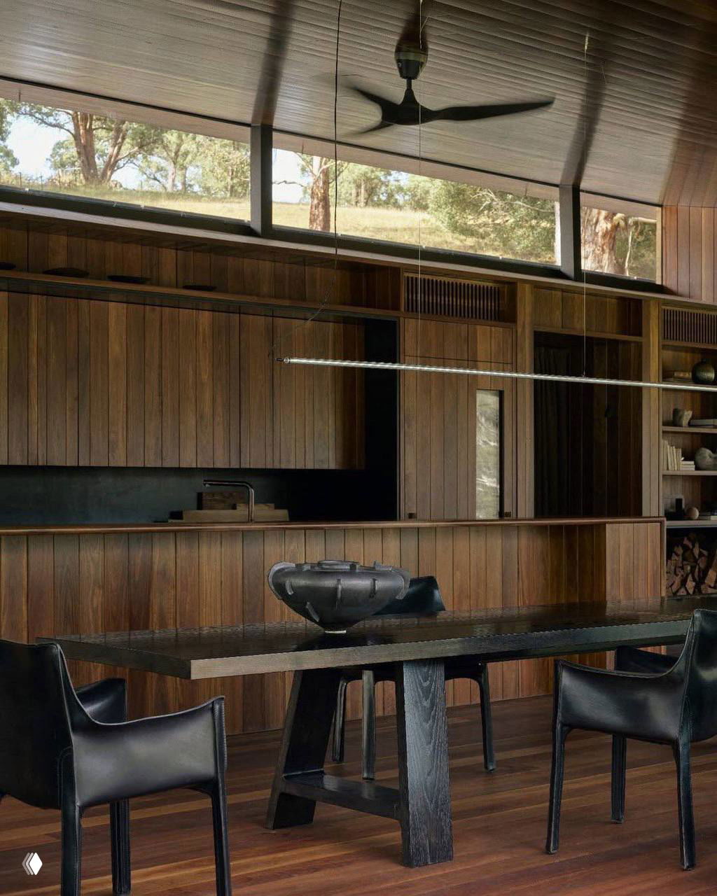 Кухонно-столовая зона с деревянными шкафами и массивным столом, строгие линии и природная палитра материалов в едином стиле интерьера.