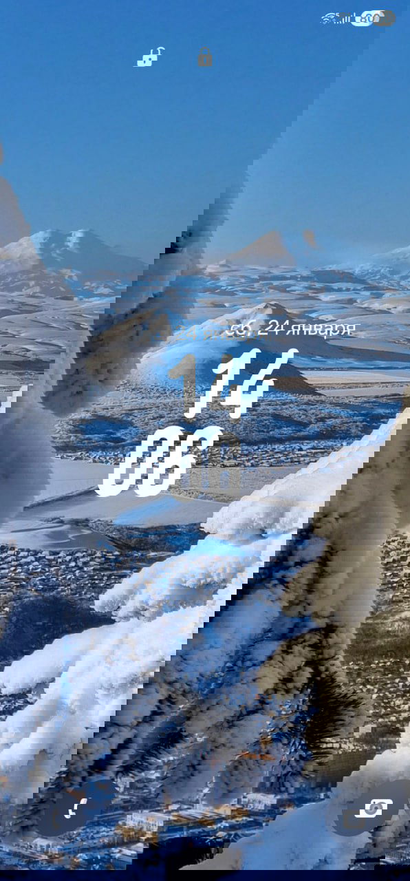 Вертикальное зимнее фото с видом на заснеженный город и гору, кадр обрамлён ветками в снегу; подходит для заставки телефона.