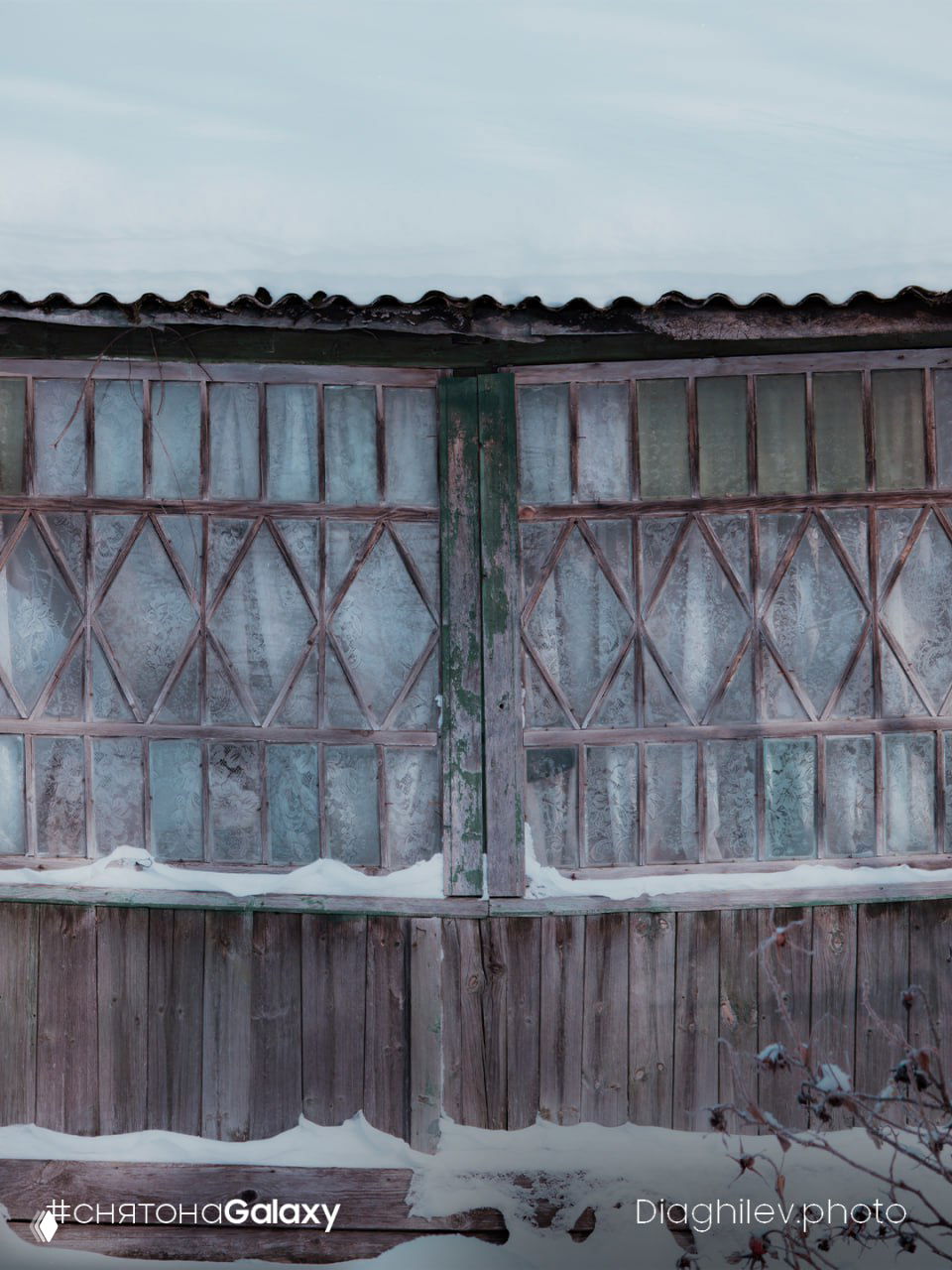Старинный деревянный фасад с замёрзшими окнами и снегом на крыше; атмосферный кадр с заметным ватермарком и подписью автора.