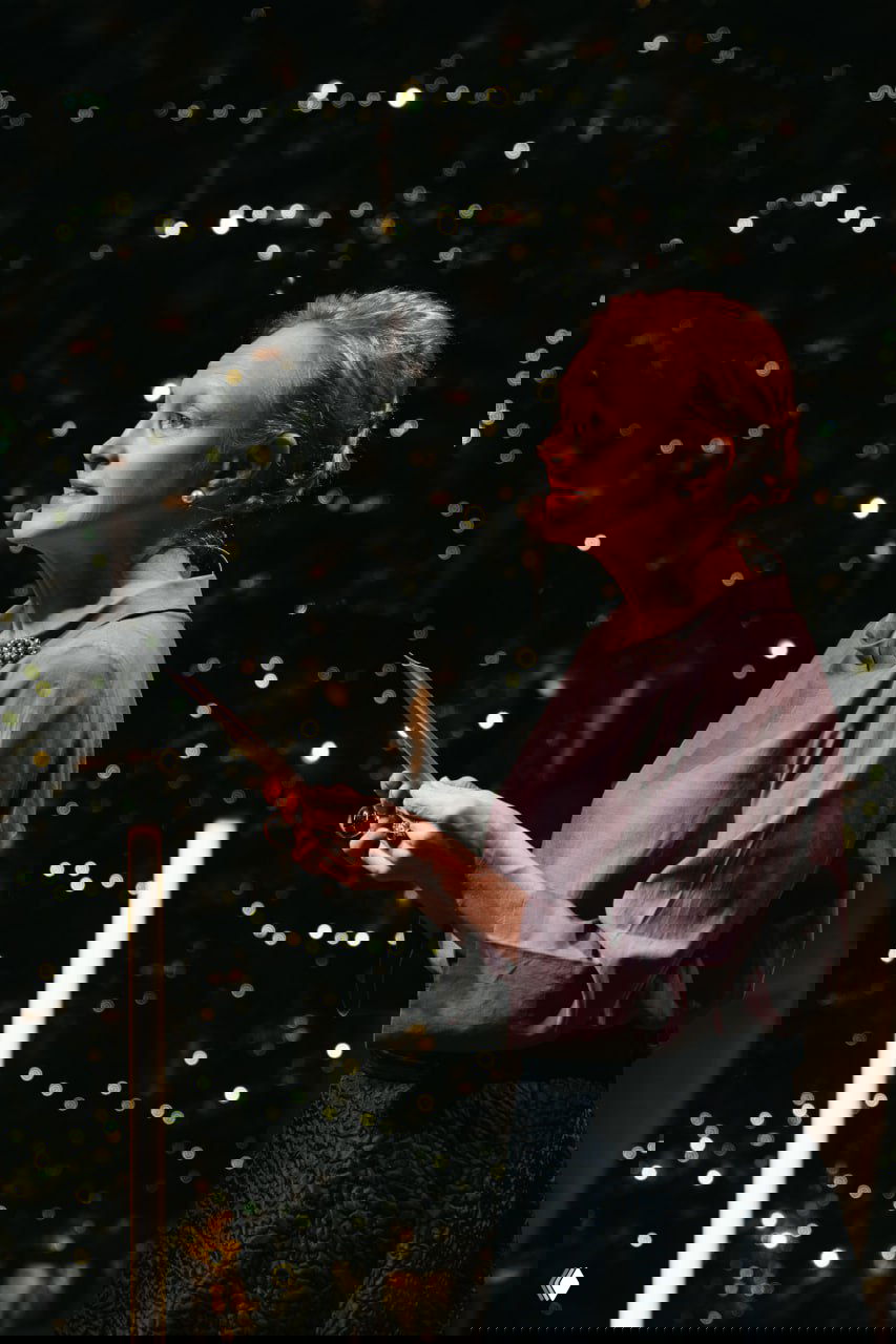 Женщина читает со сцены при мерцающем освещении и гирляндах; атмосферный кадр с выступления в рамках проекта «Живые страницы».