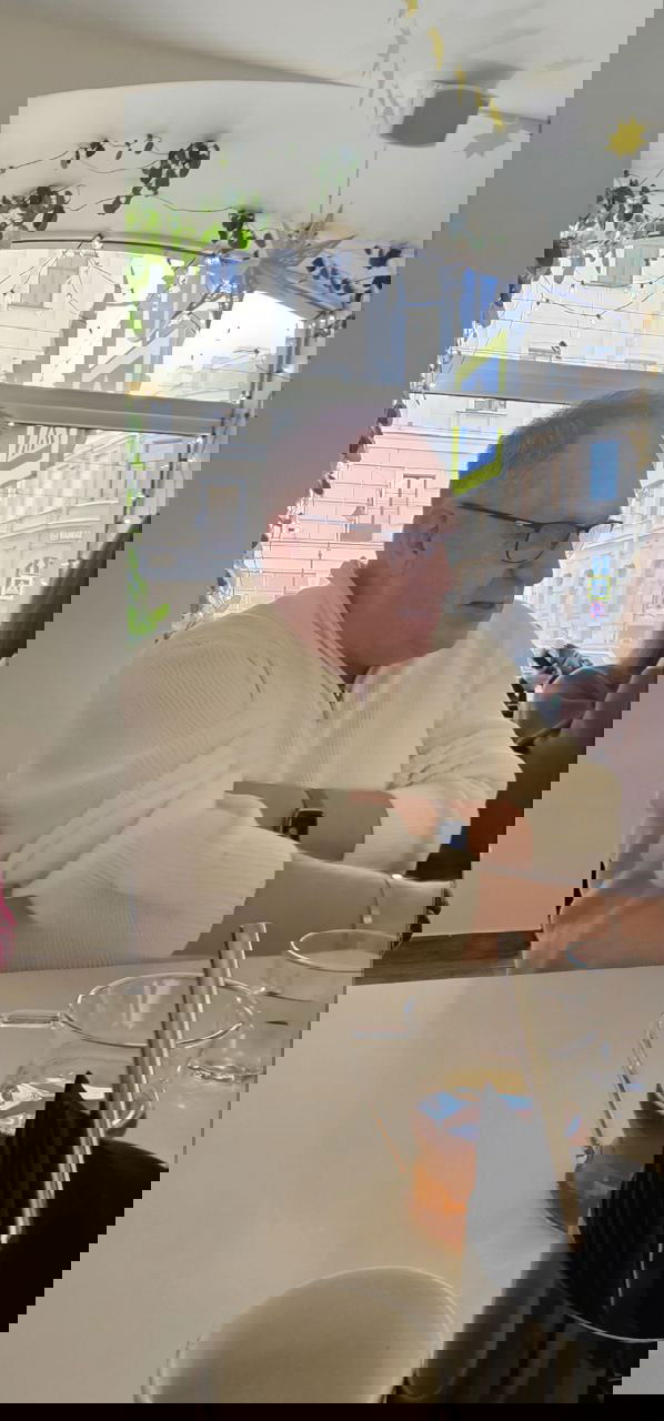 Профильный портрет Константина Харского за столом в кафе: видны чашка чая, окно с городским пейзажем Петербурга и праздничные украшения.