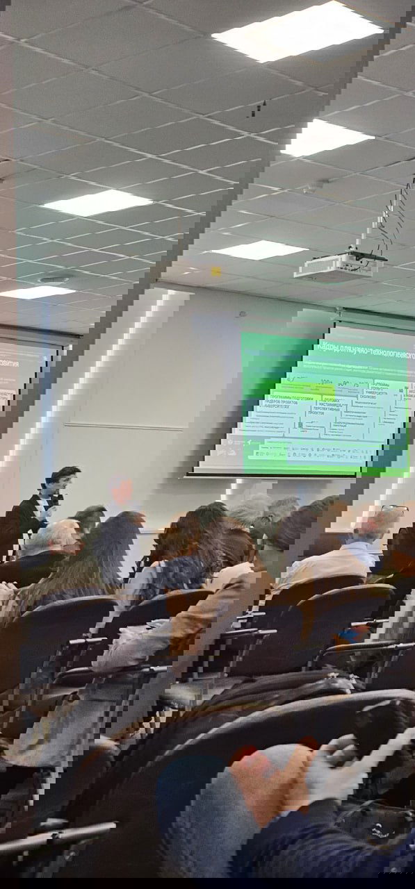 Зрительный зал мероприятия: докладчик у экрана и аудитория в креслах на Дне Сколково в петербургском технопарке, вид с задних рядов.