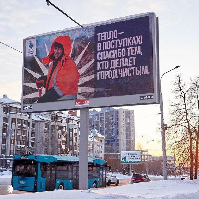 Близкий план билборда с текстом и графикой на фоне заснеженного тротуара и деревьев; у изображения видны цифровые артефакты и искажения.