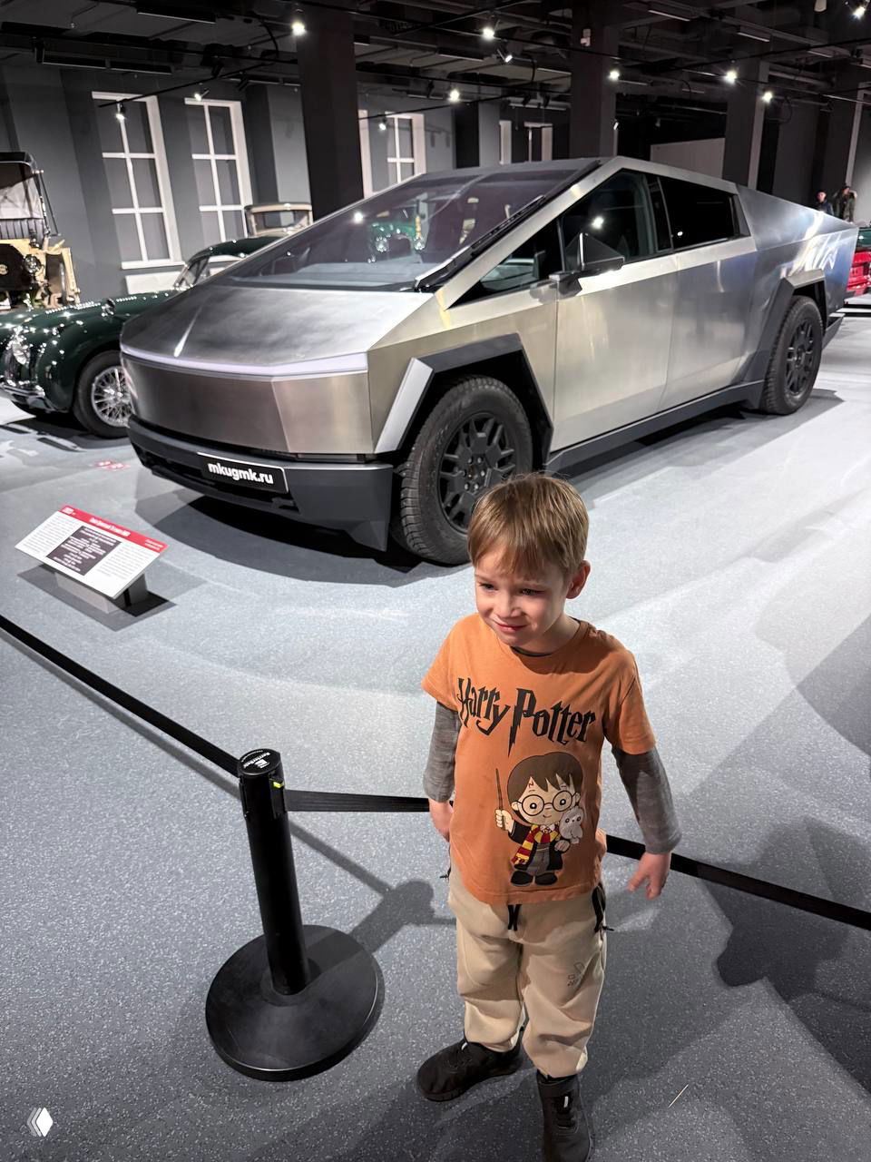 Ребёнок на фоне футуристического металлического автомобиля в просторном выставочном зале — современная часть экспозиции рядом с классикой.