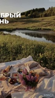 Пикник на пледе у реки: на покрывале сервировка с блюдами и букетом, уютная летняя сцена на фоне поля и берёзового леса.