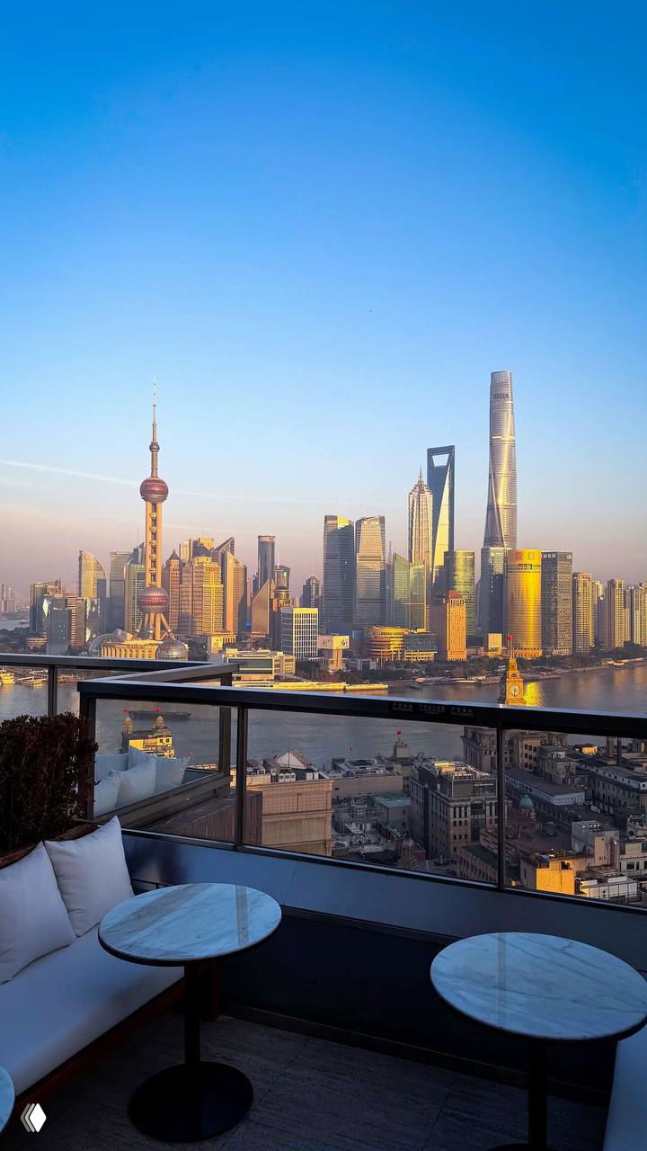 Дневной вид на панораму Шанхая с террасы: столики на переднем плане, река, высотные офисные здания и закатное освещение создают городской пейзаж.