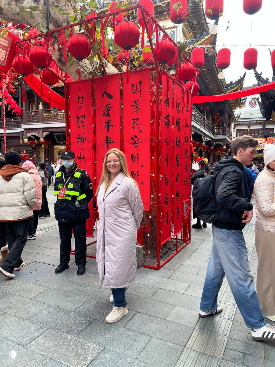 Женщина улыбается на фоне красных фонарей и праздничных декораций в шумном туристическом районе Шанхая, люди вокруг и традиционные украшения.