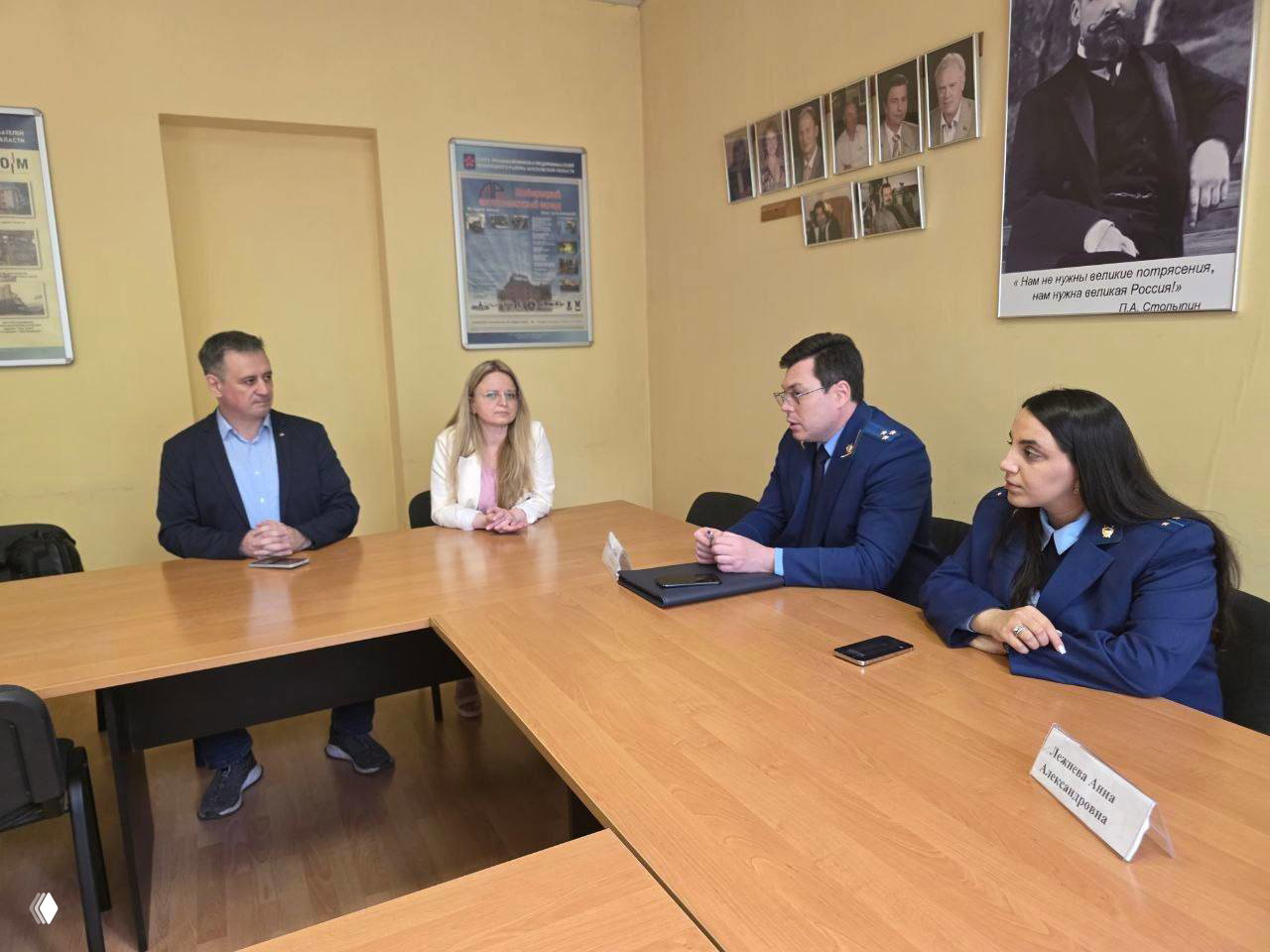 Крупный план заседания: трое участников за столом, двое в форменной одежде, обсуждение вопросов в небольшом кабинете с фотографиями на стене.