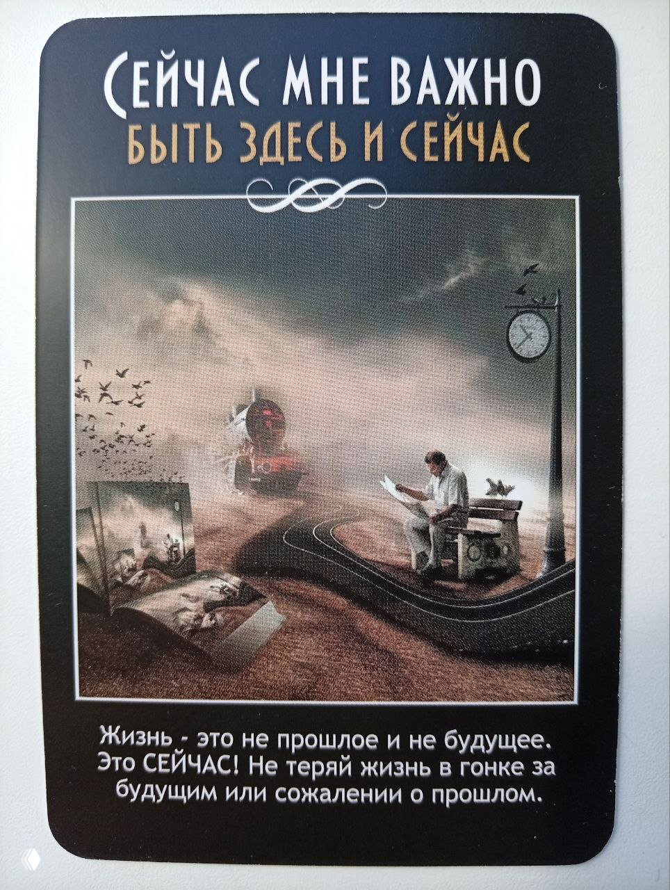 Карта с сюрреалистической сценой и текстом «быть здесь и сейчас», напоминание не терять жизнь в сожалениях о прошлом и страхах о будущем.