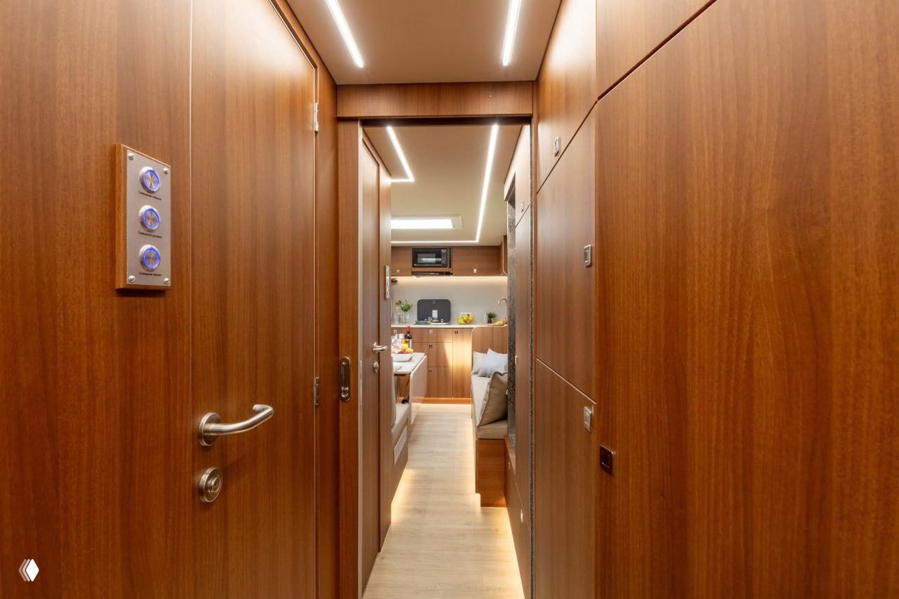 Длинный коридор внутри жилого модуля с тёплой деревянной отделкой, встроенными шкафами и точечной LED‑подсветкой по потолку и стенам.