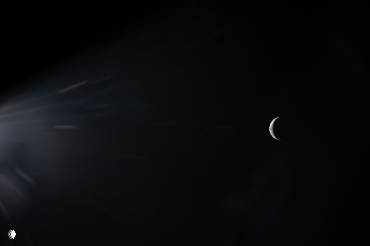 Луч света и блики слева на тёмном фоне космоса; справа — маленький серп Земли, снятый в ходе семичасового облёта Луны.