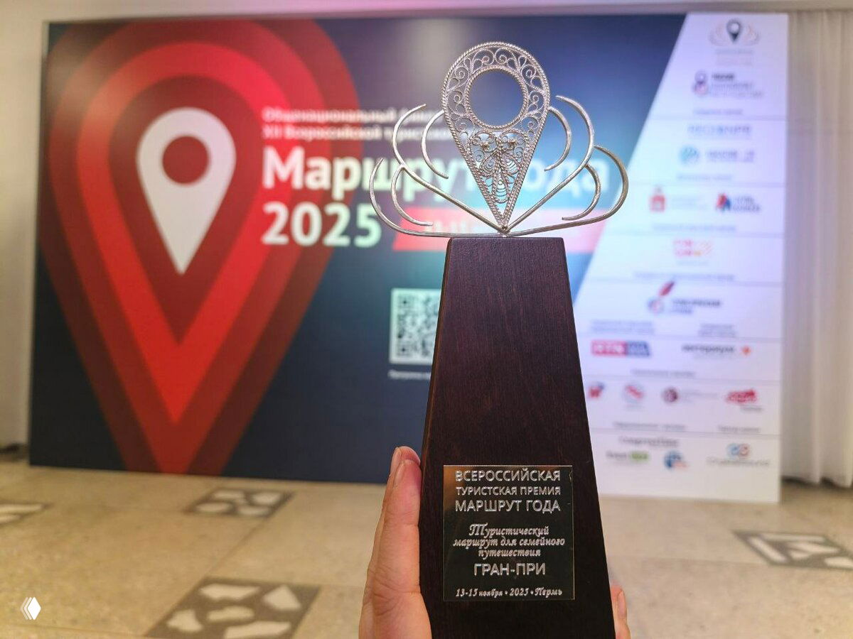 Крупный план симпатичного трофея премии «Маршрут года», в руках у человека, на размытой фоне видно бренд и оформление мероприятия в Перми.