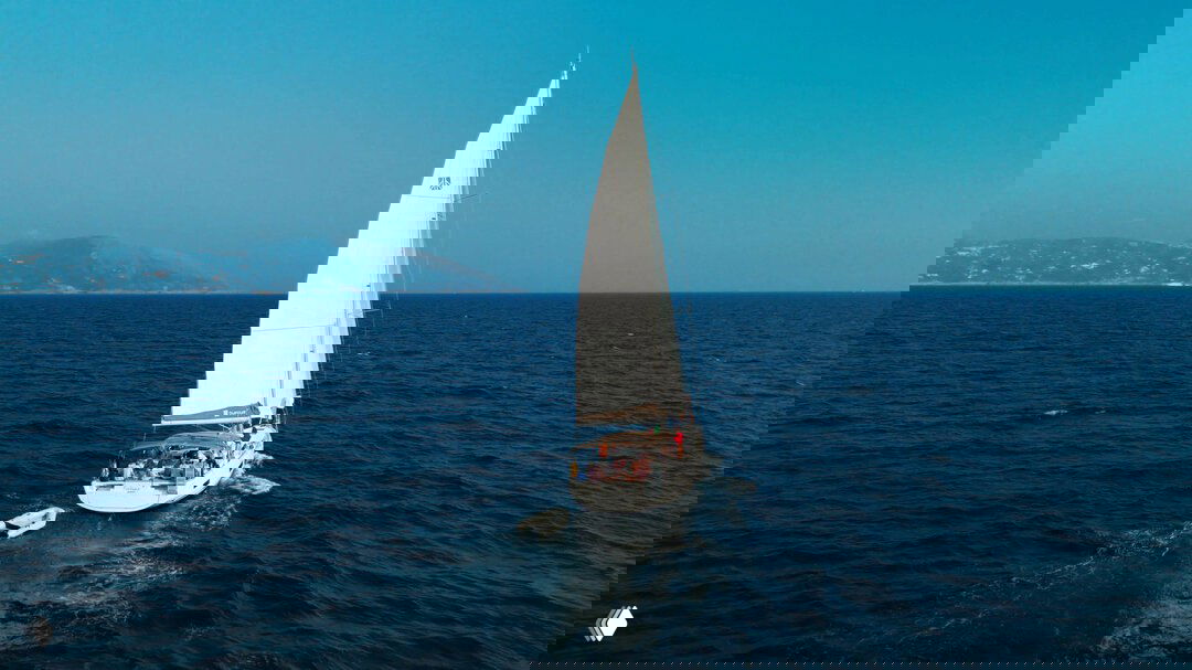 Вид сзади на яхту с поднятым парусом, вдалеке виднеется берег; кадр передаёт атмосферу морской прогулки и открытого горизонта.