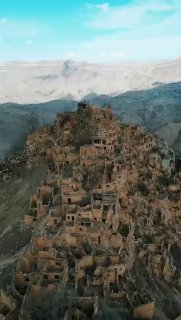 Вертикальная панорама заброшенного аула Гамсутль в Дагестане: плотные каменные руины на крутом горном склоне, скалы и пустота вокруг.