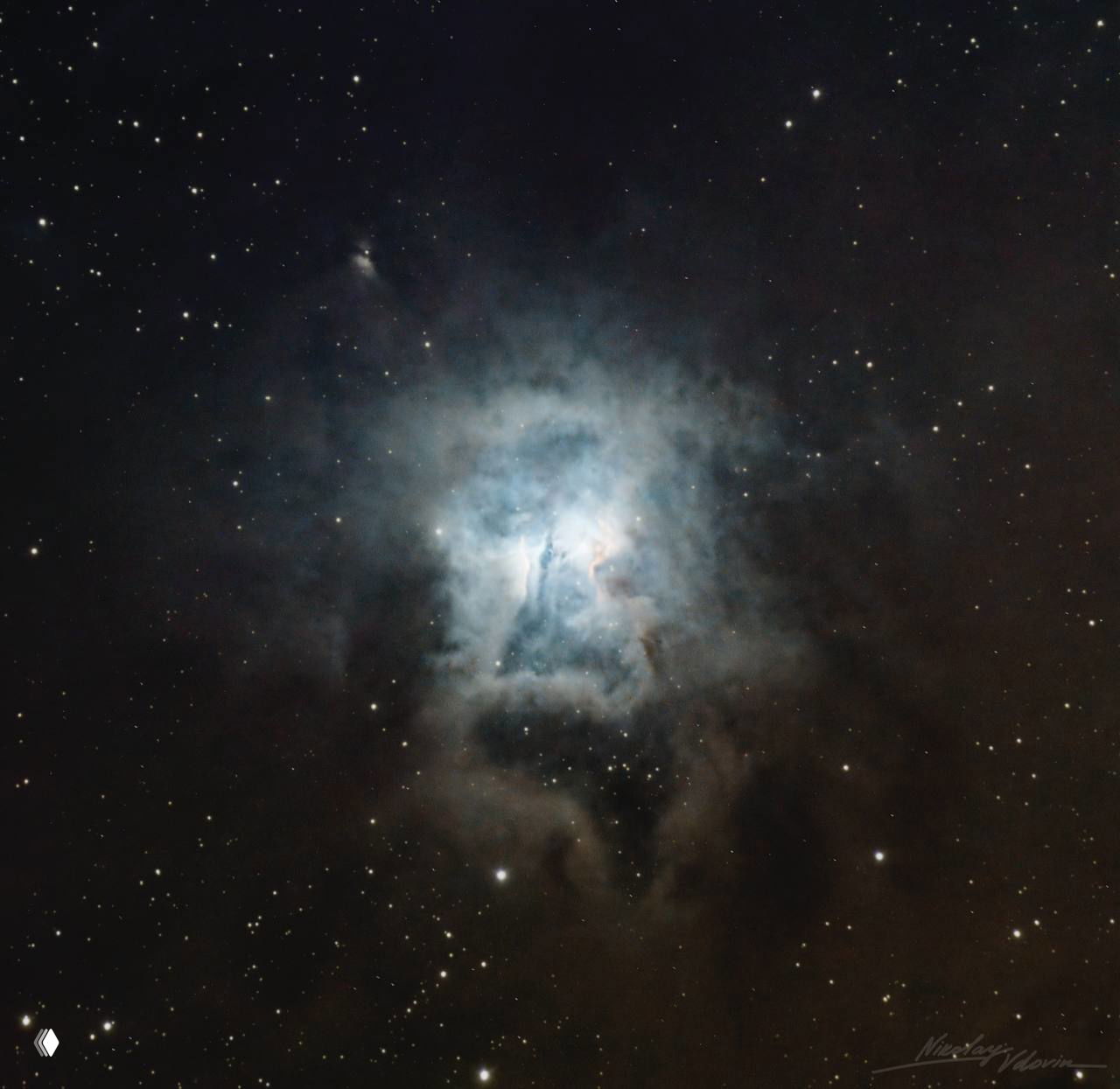 Холодное голубовато-белое свечение отражательной туманности на фоне тёмного звездного поля и локальных плотных пылевых структур.