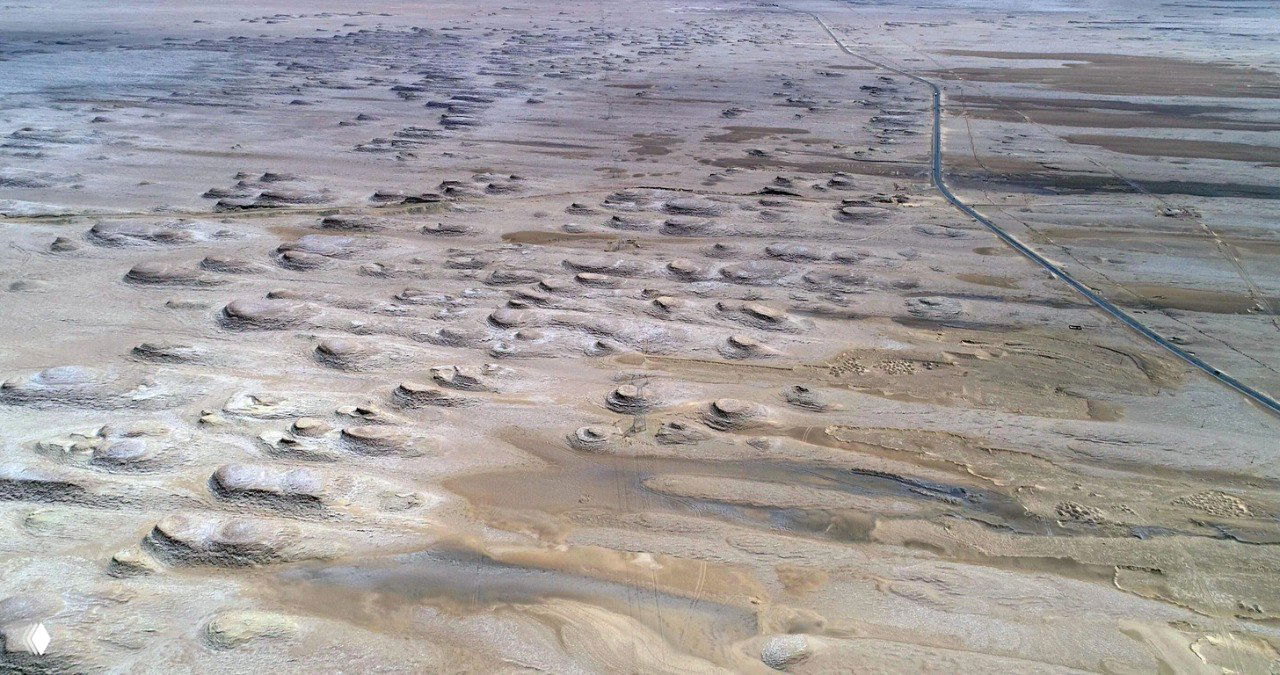 Аэрофото: дорожная трасса справа от кадра пересекает ландшафт с множеством солончаковых гряд и бугров в Цайдамской котловине.