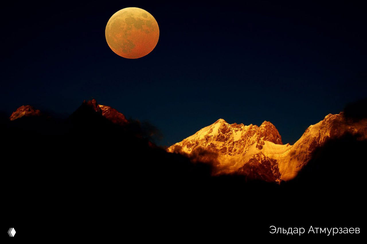 Ночное горное небо с большой луной над освещёнными вершинами; драматический кадр кавказских гор с контрастом тёплого света и тёмного неба.