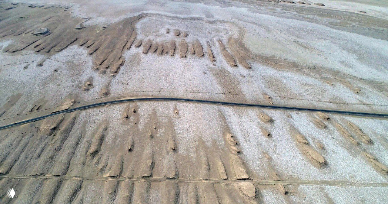 Аэрофото: ровное шоссе пересекает причудливый солончаково-песчаный рельеф Цайдамской котловины, заметны полосы соли и песка.