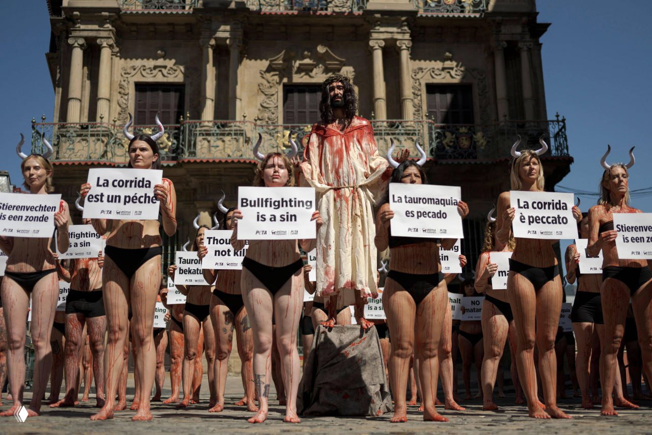 Акция протеста против корриды: люди с табличками «Bullfighting is a sin» и сценической инсталляцией, участники покрыты краской для выразительности протеста.