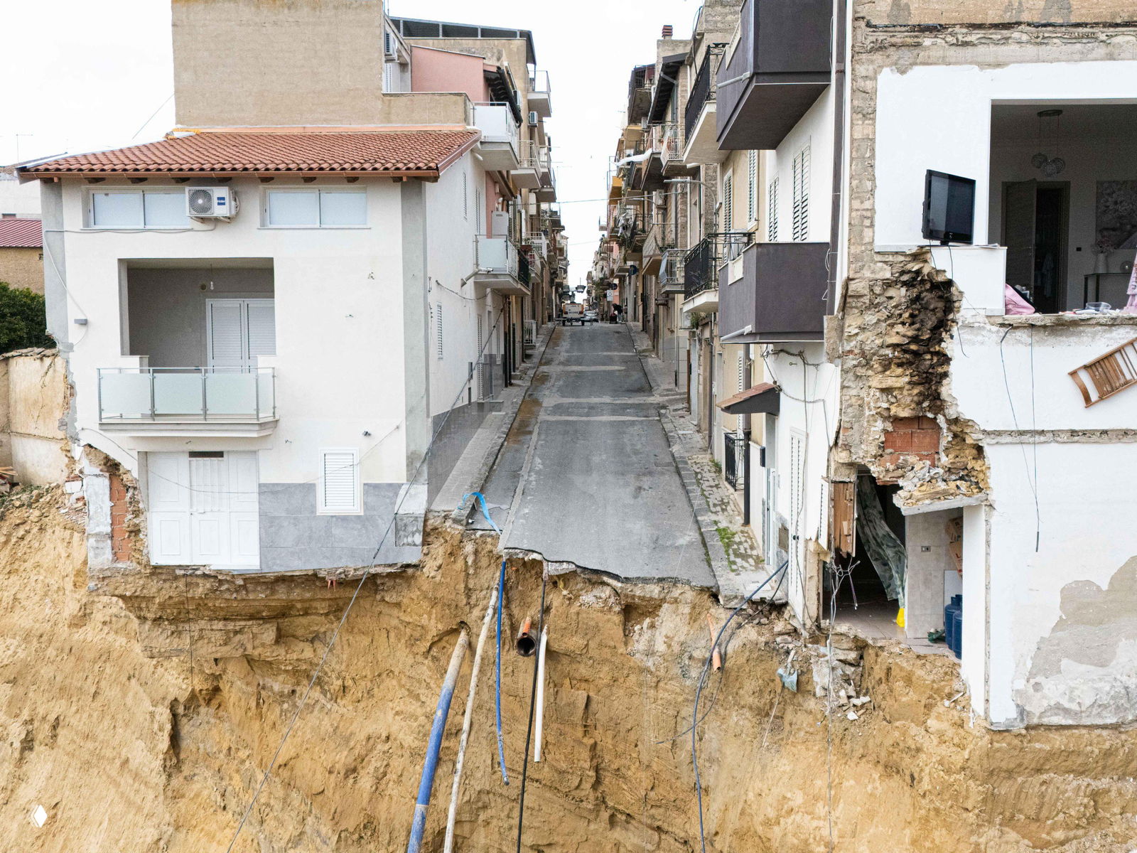 Крупный план: обрушившаяся часть улицы в Нишеми, асфальт и коммуникации оборваны, видны разломы фундамента и торчащие трубы.