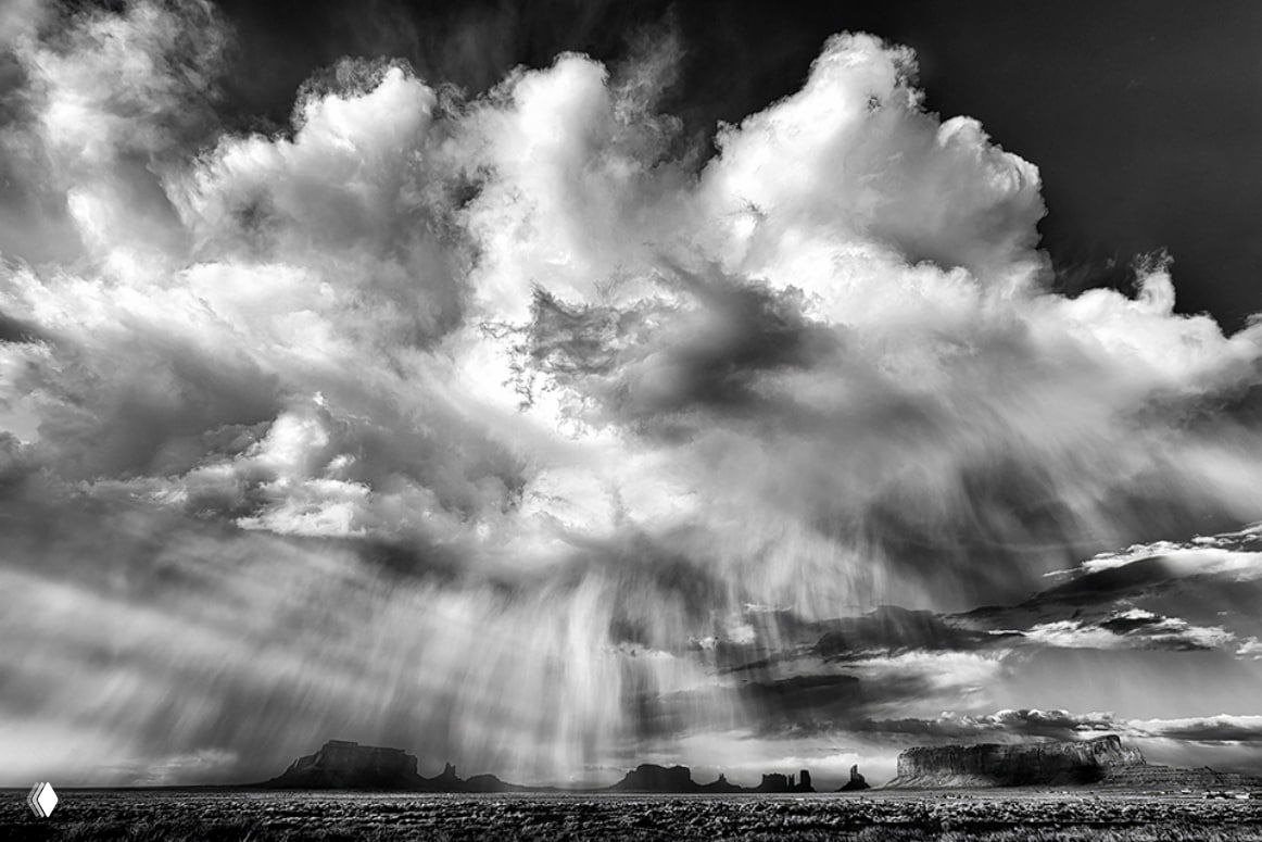 Монохромный драматичный пейзаж Аризоны: массивные облака над плоскогорьем и силуэтами скал, дождевые потоки и высокий контраст света и тени