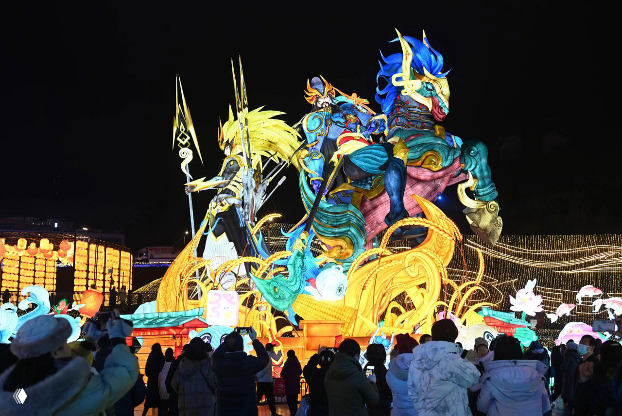 Массивная световая скульптура в виде мифологического всадника и декоративные элементы вокруг — посетители фотографируются на фоне яркой подсветки инсталляции.