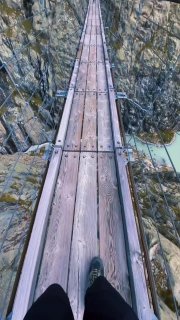 Вид вниз по деревянной настилке подвесного моста Трифт: узкая тропа между скалами, внизу виднеется бирюзовое озеро, в кадре видны ноги автора.