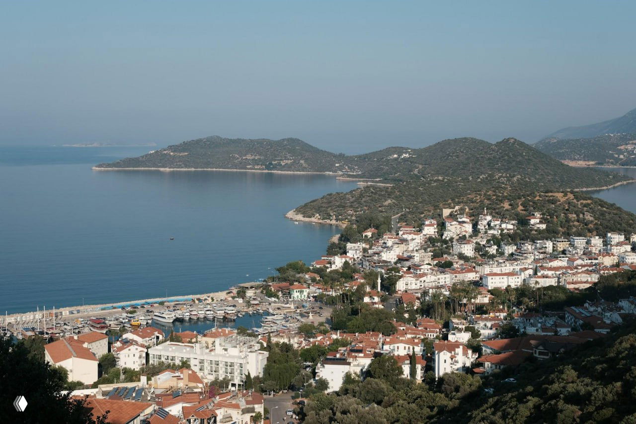 Вид с высоты на плотную прибрежную застройку Каша, набережную и бухту с небольшими лодками — уютный приморский ландшафт.