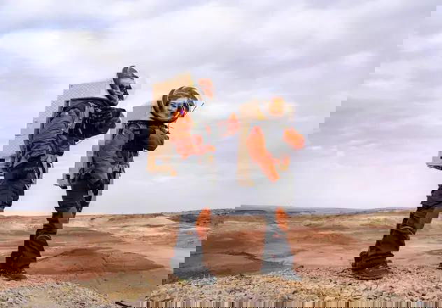 Два человека в оранжевых скафандроподобных костюмах с рюкзаками‑блоками на фоне марсианоподобного ландшафта Гоби — участники симуляции в экипировке.