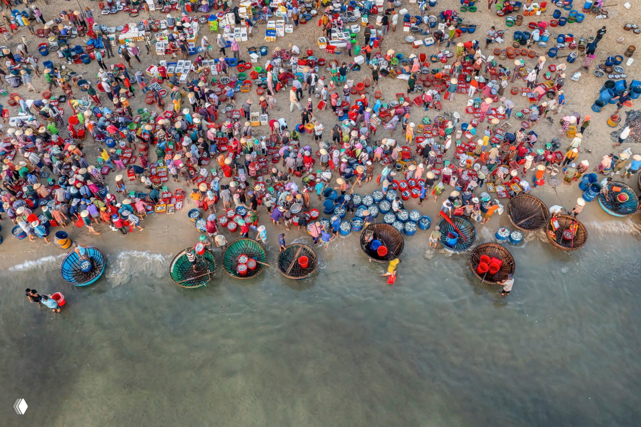Широкий вид на пляжный рынок Там Тьен: плотная скопление людей, корзин и лодок у берега — оживлённый утренний рыбный рынок Вьетнама.