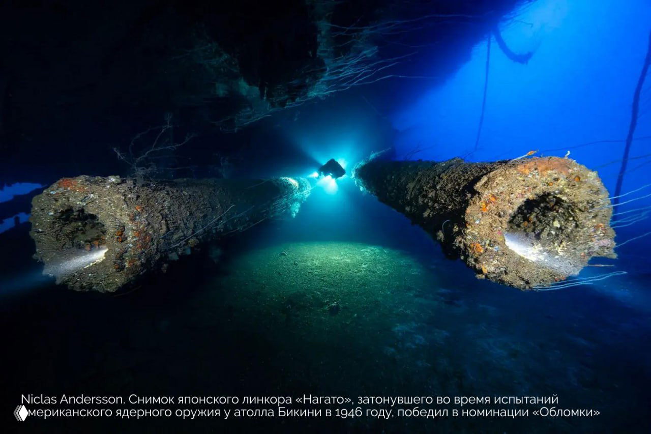 Кадр затонувшего корабля на фоне голубого света: руины линкора, колонны и атмосфера подводного крушения в широком плане.