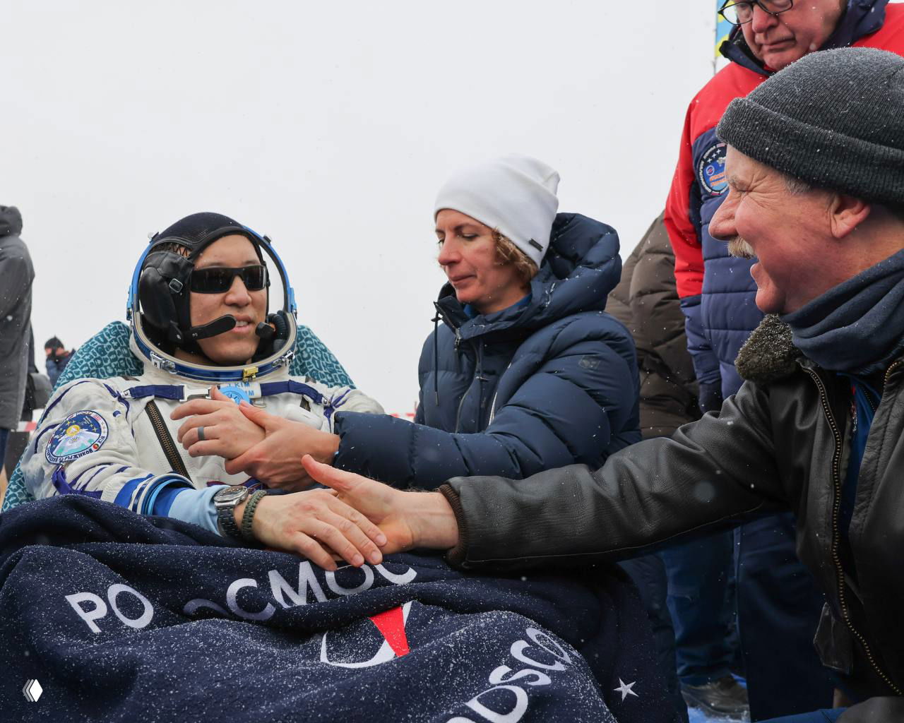 Астронавт Джонатан Ким после возвращения под одеялом Роскосмоса: окружён сотрудниками и волонтёрами, которые приветствуют и помогают члену экипажа.