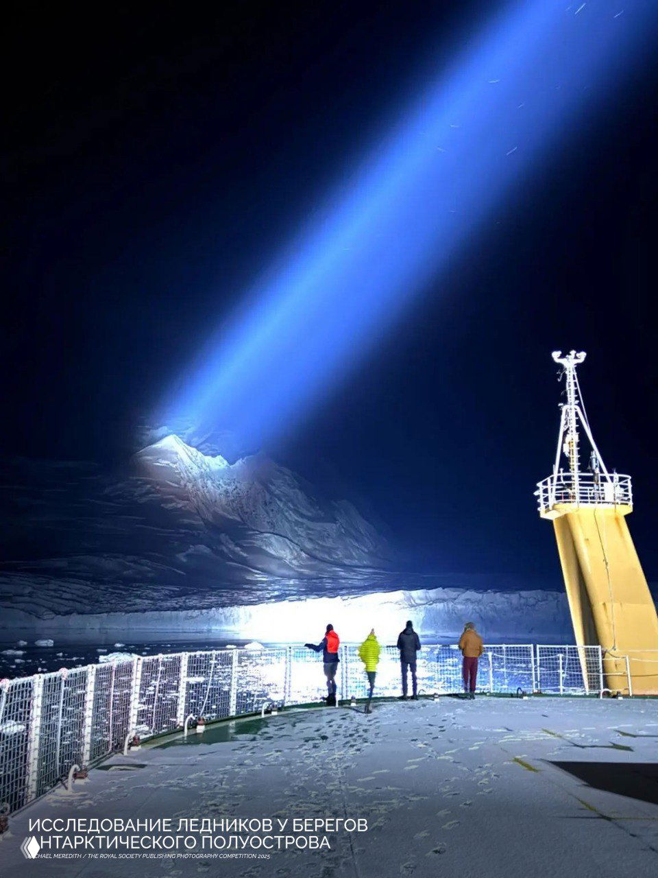 Ночная полярная сцена с судном у айсберга и направленным с палубы ярким прожекторным лучом на ледяной склон — исследование льдов у побережья полуострова.