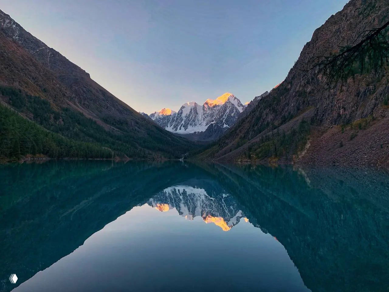 Тихая гладь Шавлинского озера в узкой горной долине Алтая, зеркально отражающая вершины и создающая эффект уединённого высокогорного пейзажа.